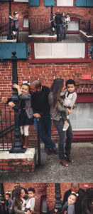 Ybor City family photography showing daughter climbing iron gate post, full family portrait against brick wall with blue shutters, candid parent and children moments