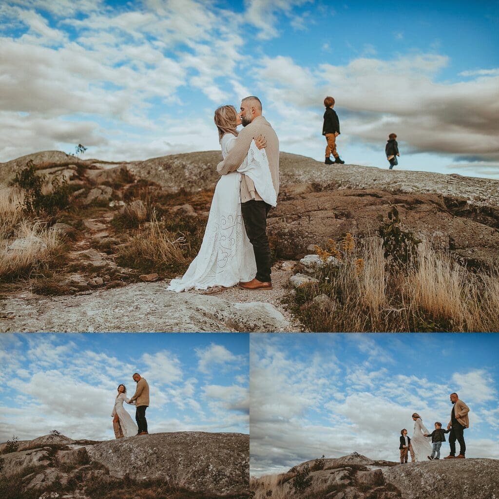 Family portrait on rocky mountain peak with vast valley landscape below, children playing with flowing white fabric, dramatic sky and sweeping mountain vista backdrop