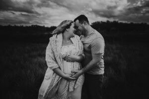 Black and white maternity photo of partner embracing expectant mother from behind with hands on bump